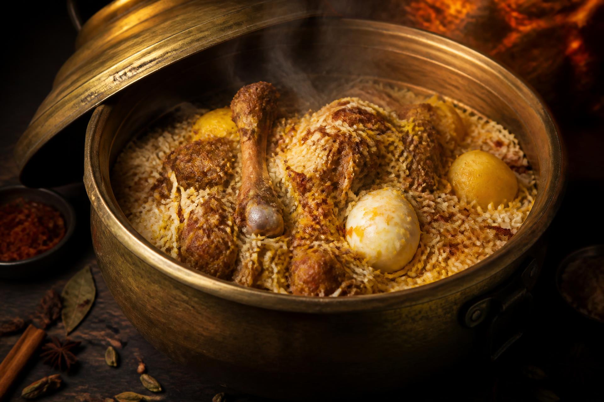 Sealed brass handi of Dhaka-style mutton kacchi biryani opened, steam rising over saffron rice